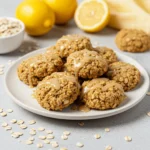 A plate of lemon oatmeal no bake cookies with a drizzle of lemon glaze and fresh lemon slices in the background.